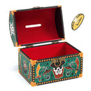 A vibrant Pirate Money Box from Djeco features a pirate-themed treasure chest with an open lid, decorated with skulls and swords along its sides. This wooden piggy bank boasts a red interior and a convenient slot on top for collecting savings. Adjacent to it, a gold coin seems to hover, enticing adventurers to contribute to their collection in this pirate money bank.