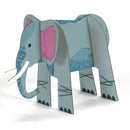 Introducing the "Colour, Assemble & Play - Savannah" set by Djeco, a creative kit that includes a cardboard cutout of an elephant featuring a light blue body and pink ears adorned with simple doodle-style designs. This fun savannah animal stands upright and includes easy-to-find slots for effortless coloring and assembly.