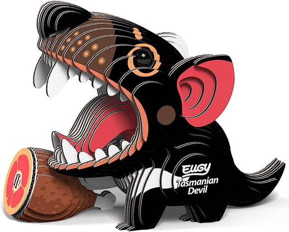 A vibrant, cartoon-style Tasmanian Devil from the EUGY brand, made from biodegradable layered cardboard, features its mouth open wide and holds a cartoon ham with a bone in its paw. This eco-friendly design is labeled "Eugy Tasmanian Devil.