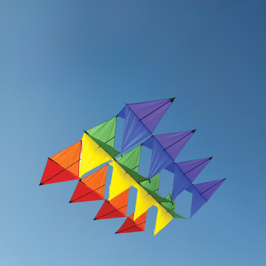 The SPIRIT OF AIR Aurora Box Kite features vibrant multi-tier triangular sails in red, orange, yellow, green, and purple. Its sturdy glass fiber frame ensures effortless flying against a clear blue sky for enthusiasts of all ages.