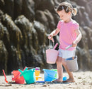 Child playing on a beach with colourful sand buckets and toys.
