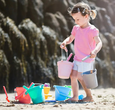 Child playing on a beach with colourful sand buckets and toys.