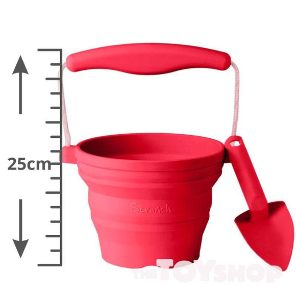 The SCRUNCH Mini Bucket & Spade, ideal for young gardeners, is a red collapsible silicone bucket with a handle and small red spade attached. It's labeled "Scrunch," stands 25 cm tall, and is perfect for creative outdoor play.