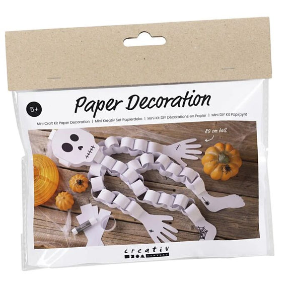 A package labeled "Mini Craft Kit Paper Decorations, Skeleton" from Creativ Company contains a children's craft kit to create a paper skeleton made of white strips—perfect as a Halloween decoration. Designed for ages 5 and up, it includes illustrations of the completed skeleton adorned with small pumpkins.