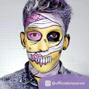 A creative Halloween look features a mummy-like face with yellow skin, purple highlights using Snazaroo Face Paints by SNAZAROO, wrapped in white bandages. One eye is blacked out; the mouth shows detailed teeth. The person wears a denim jacket.