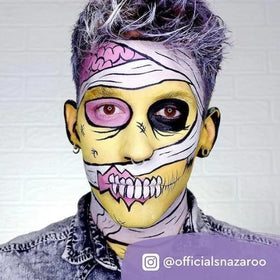 A creative Halloween look features a mummy-like face with yellow skin, purple highlights using Snazaroo Face Paints by SNAZAROO, wrapped in white bandages. One eye is blacked out; the mouth shows detailed teeth. The person wears a denim jacket.