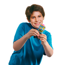 A smiling child in a blue shirt holds a small, colorful "Squeeze Popper: Zombie" figurine by Cheatwell Games, featuring sharp teeth and a mischievous expression. Ideal for both indoor and outdoor play, this toy captures the playful design against a plain white background.