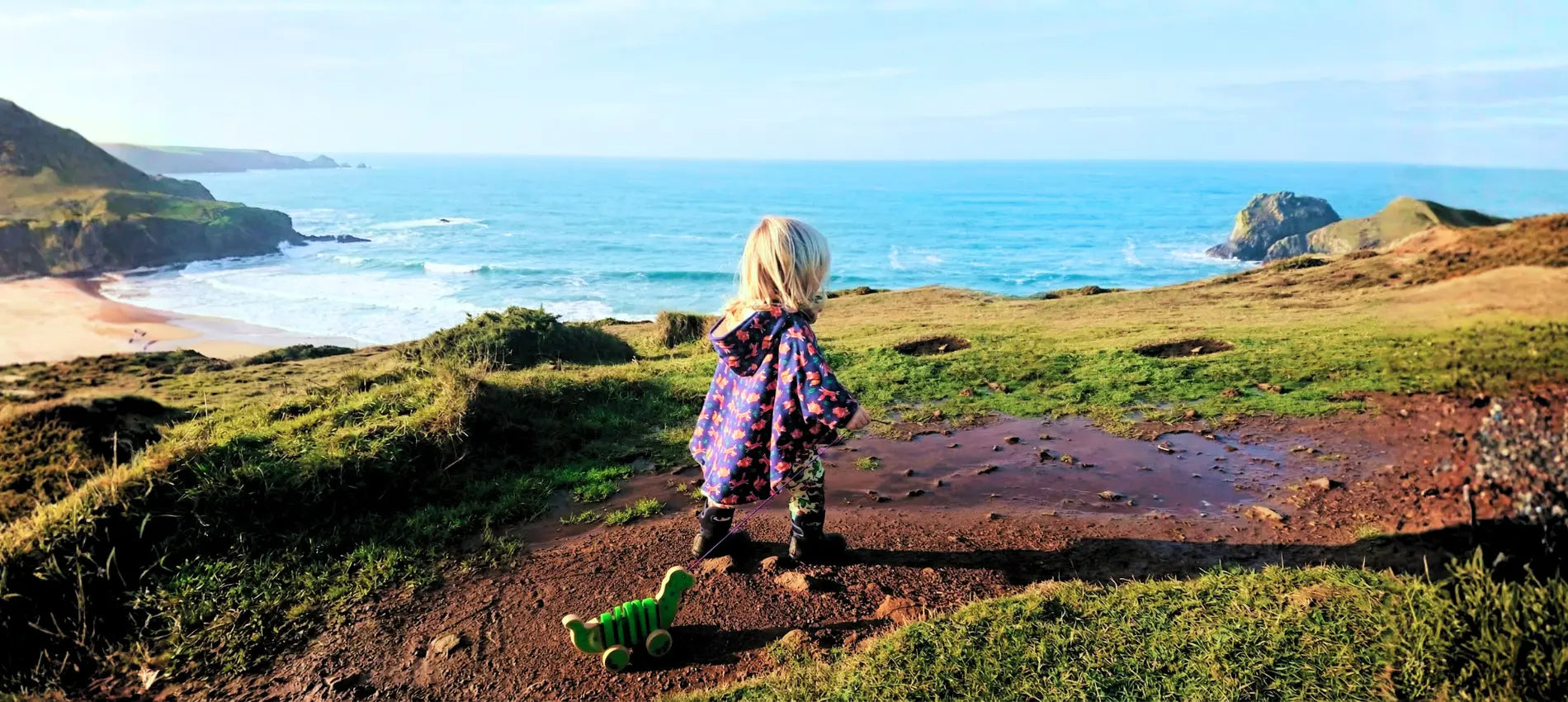 Child standing on a grassy path overlooking a coastal landscape with ocean and cliffs.