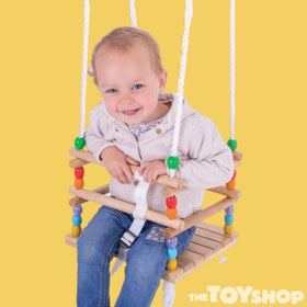 Small child in wooden cradle swing. Yellow background.