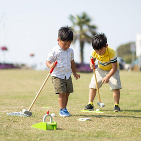 Two young, dark-haired boys one in a yellow shirt playing garden crazy golf.