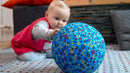 Baby reaching for a ballon encased in the blue patterned balloon cover.