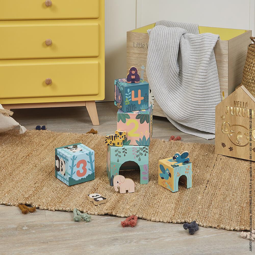 Colourful cardboard cubes stacked on a brown jute rug with yellow chest of drawers in the background.