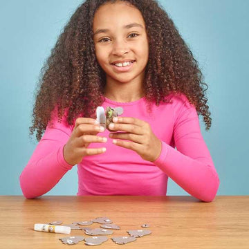 Girl in long sleeved pink t-shirt putting the cardboard parts of the koala figure together.
