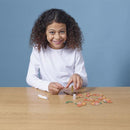 Girl smiling, wearing white long sleeved top putting pieces of craft mermaid figure together.