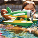 Boy playing with green and yellow seaplane as it floats on water.