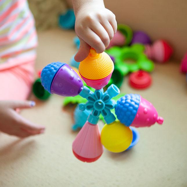 Child's hands holding large colourful play beads joined together.