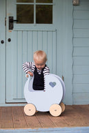 Small child in front of a light blue door with a pale blue Moover dolls' pram.