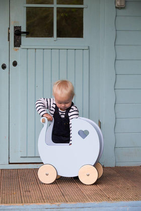 Small child in front of a light blue door with a pale blue Moover dolls' pram.