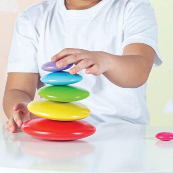 Child balancing wooden rainbow pebbles.