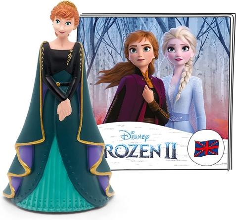 Figure of Anna from Frozen II wearing a long green cape with the booklet from the Tonie product behind. The booklet depicts the faces of Elsa and Anna from the film.