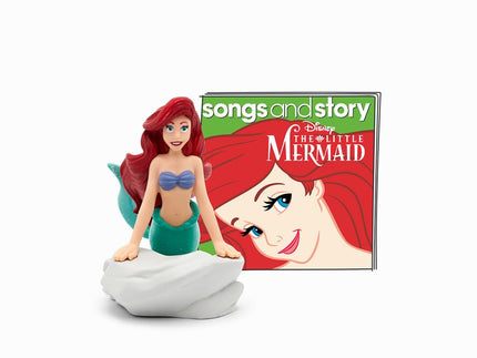 An Ariel figurine from Disney's "The Little Mermaid," part of the Tonies collection, is sitting on a rock in front of a "Songs and Story" book. With her iconic red hair, purple seashell bikini, and green mermaid tail, Ariel complements the Toniebox perfectly while her face adorns the book cover behind her.