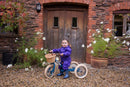 Child wearing a purple rainsuit on a green Trybike in front of a red brick house.